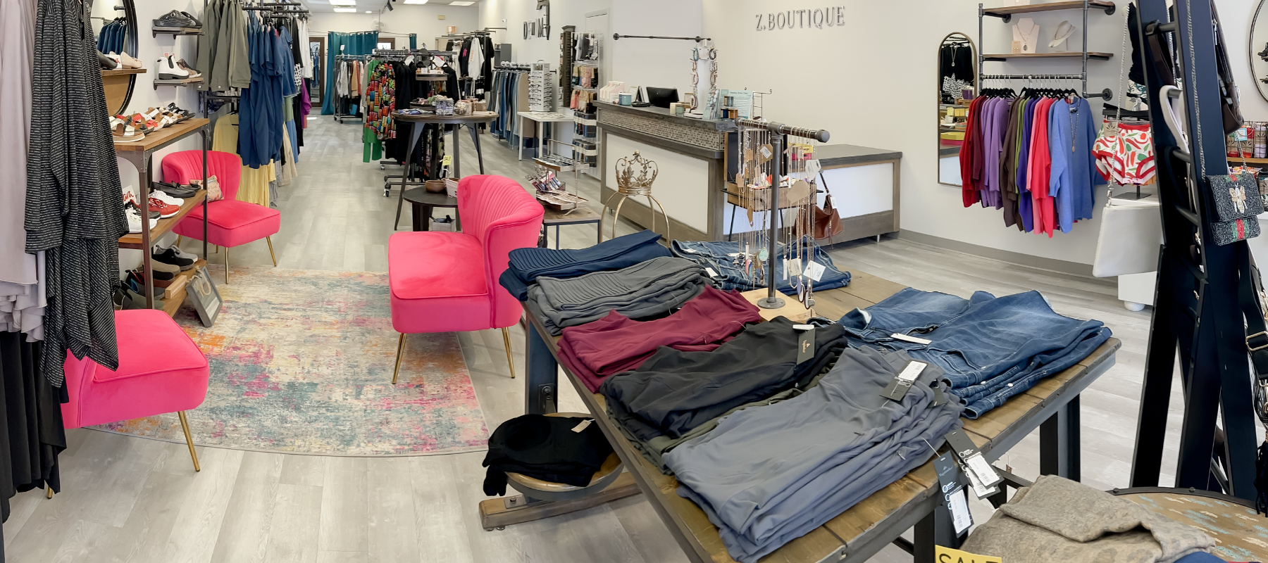 A photo of the inside of Z Boutique featuring a table with folded plus-size leggings and jeans, pink chairs, a shoe sections and various other plus-size clothing and accessories.