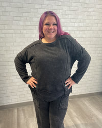 Person wearing a dark gray outfit against a light brick wall.