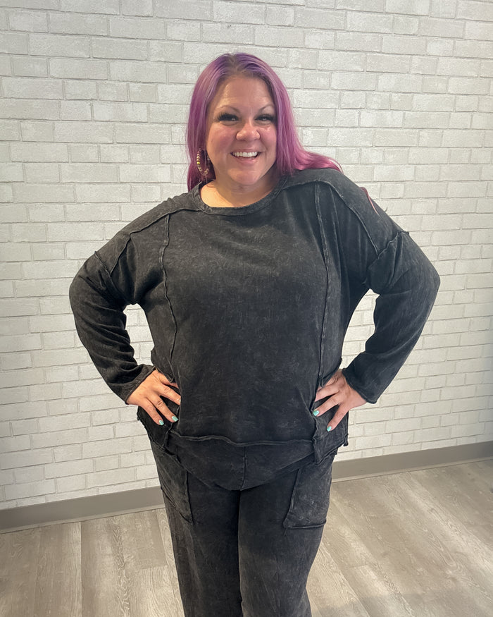 Person wearing a dark gray outfit against a light brick wall.