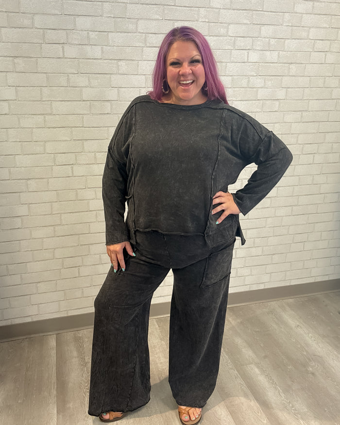 Person wearing a black outfit standing against a light brick wall.