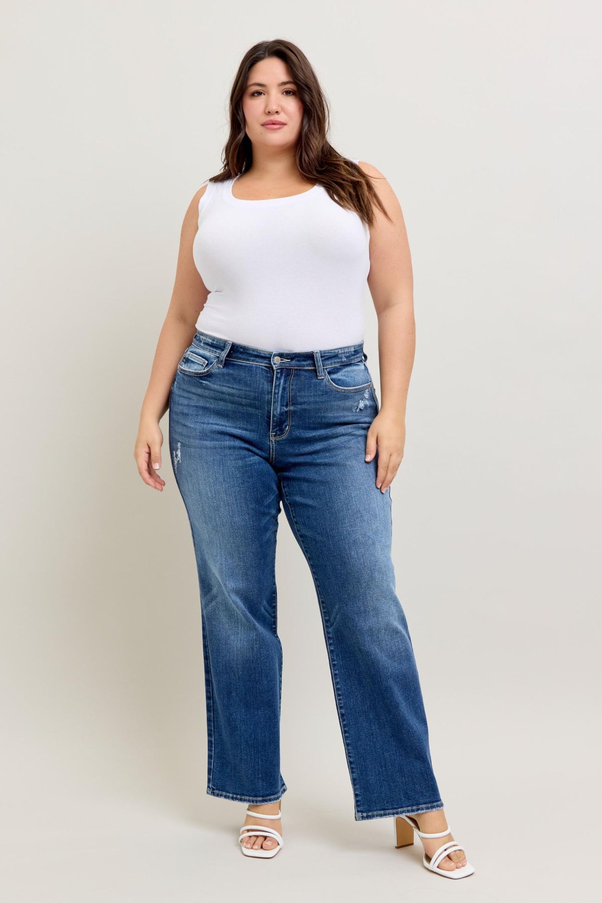 Woman wearing blue jeans and a white top against a plain background