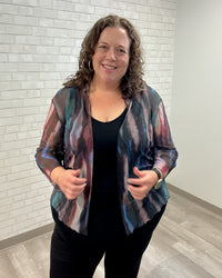 Woman wearing a colorful jacket over a black top against a white brick wall.