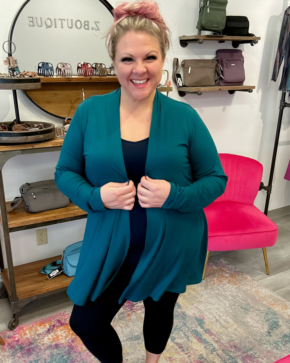 Woman wearing a teal cardigan in a store setting with shelves and bags in the background.