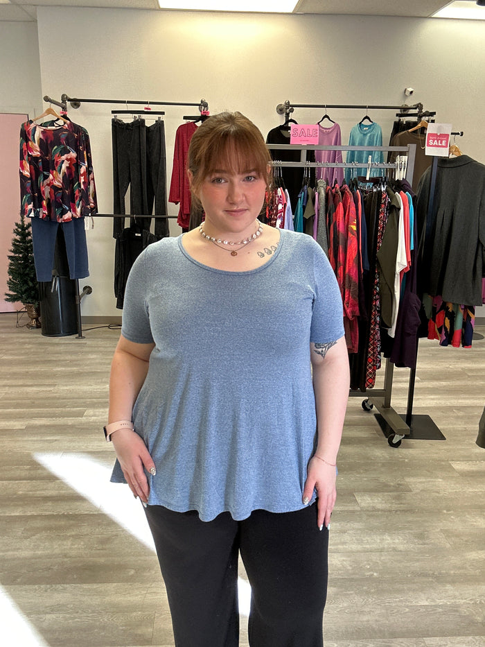 Woman in a blue sweater standing in a clothing store with racks of clothes in the background.