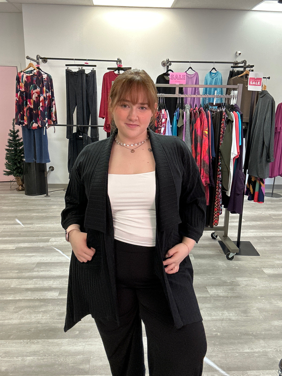 Person standing in a clothing store with racks of clothes in the background