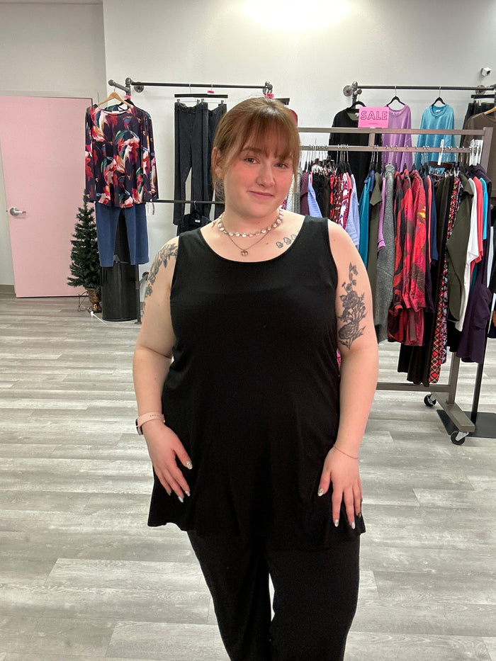 Person wearing a black dress standing in front of a clothing rack with various garments.