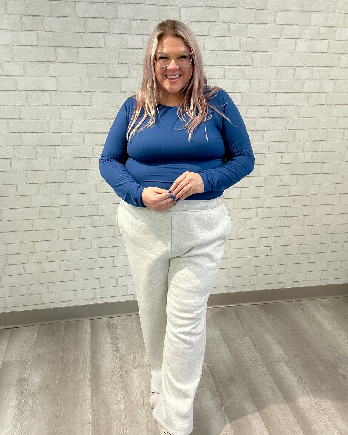 Person wearing a blue top and white pants standing against a light brick wall.