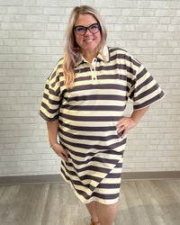 Woman wearing a striped dress standing against a light brick wall.