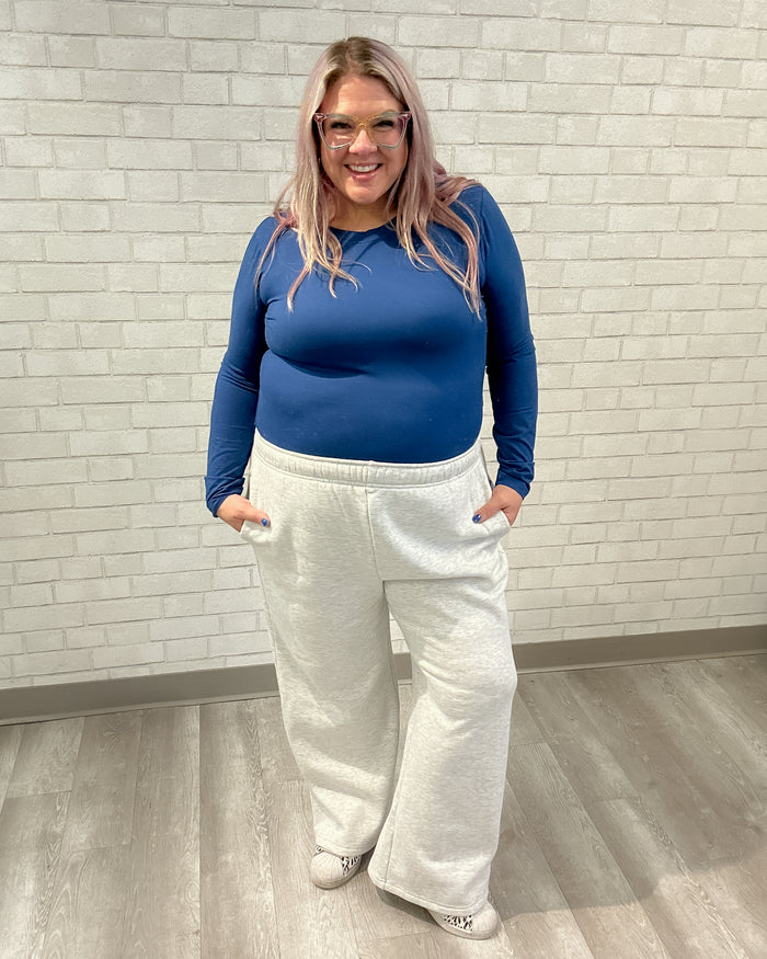 Person wearing a blue top and white pants standing against a light brick wall.